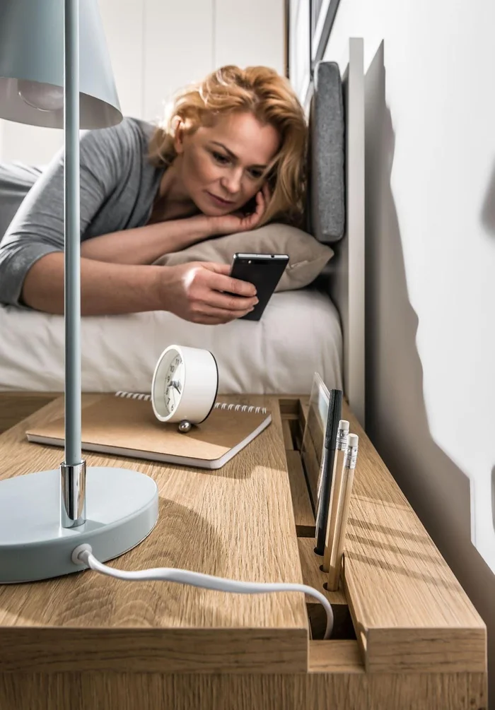 Kobieta sięga z łóżka po telefon